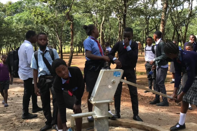 In this photo, Zambian girls and boys wash their hands to protect against the coronavirus and fill their water bottles from a borehole water pump at Ndingindi Primary School in Nakonde District of Muchinga Province.